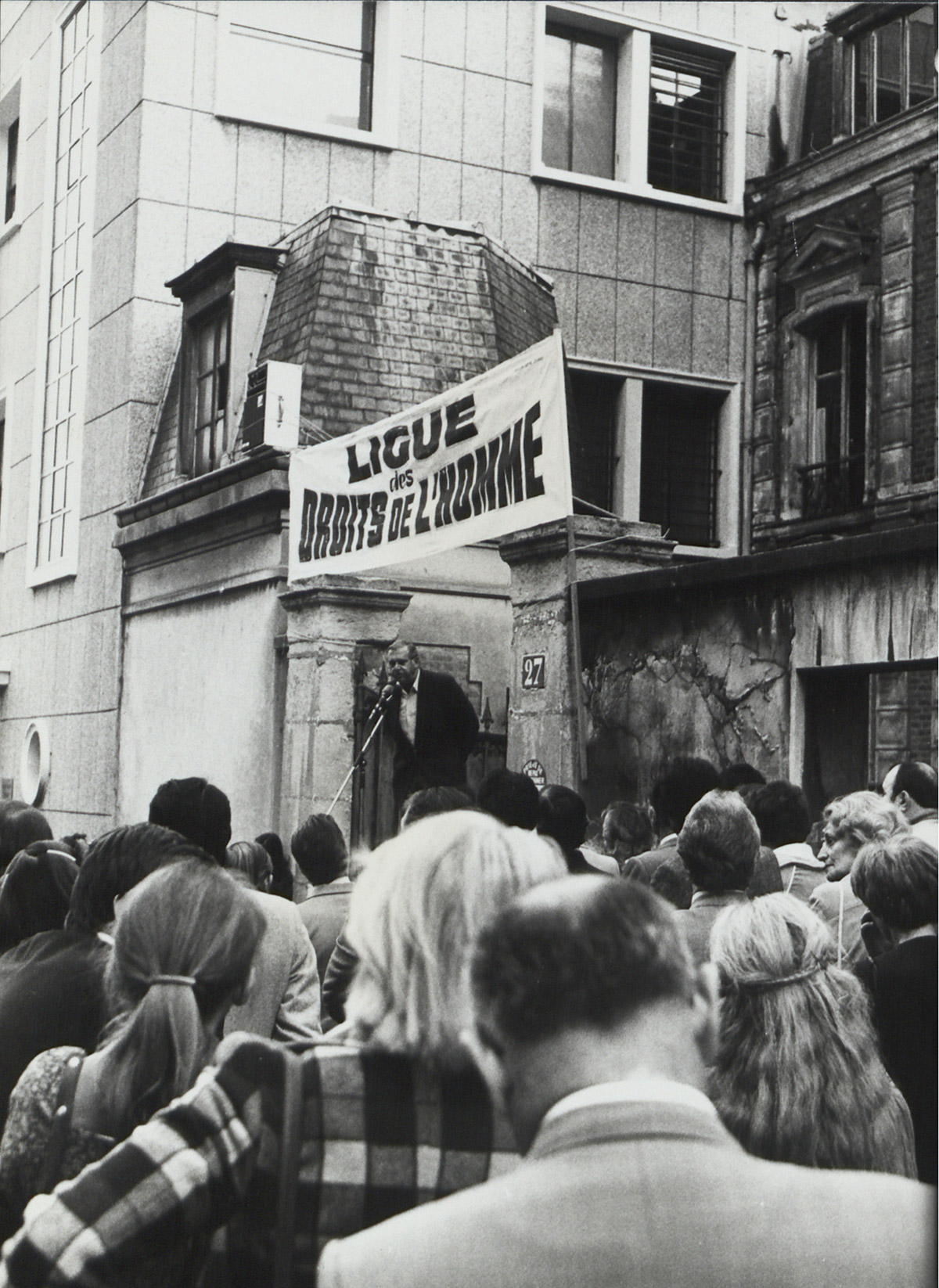 Henri Noguères, président de la Ligue de 1975 à 1984, allocution devant le siège de la Ligue, rue Jean Dolent, photographie, ca.1977